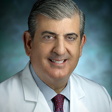 Nicholas Theodore, in a formal portrait, wearing a white lab coat, red and blue tie and light blue button down shirt
